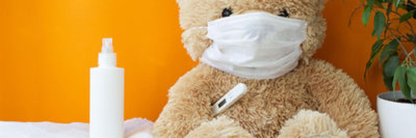 A teddy bear wearing a mask and holding a thermometer.