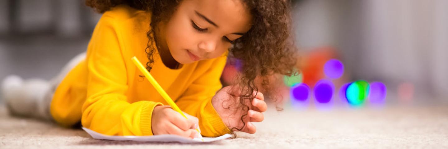 Photo of child writing on paper while laying down