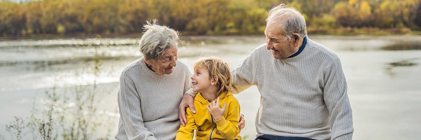 Photo of Senior grandparents sitting with grandson by lake