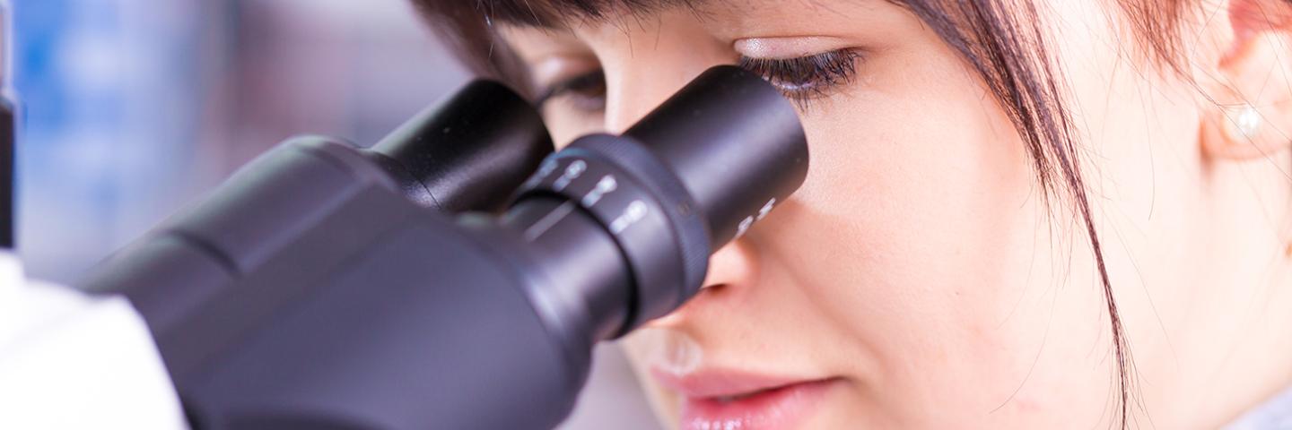Photo of a women working on a microscope in a lab