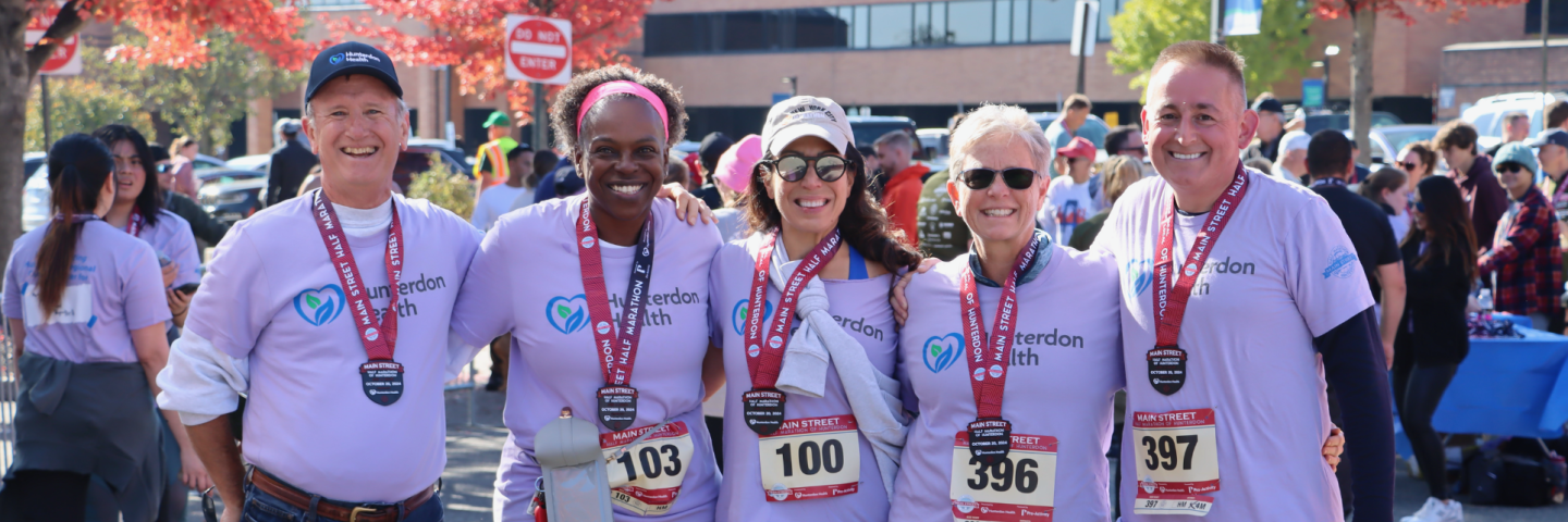 Hunterdon Health Board Members and friends smile under finish line at Main Street Half Marathon of Hunterdon