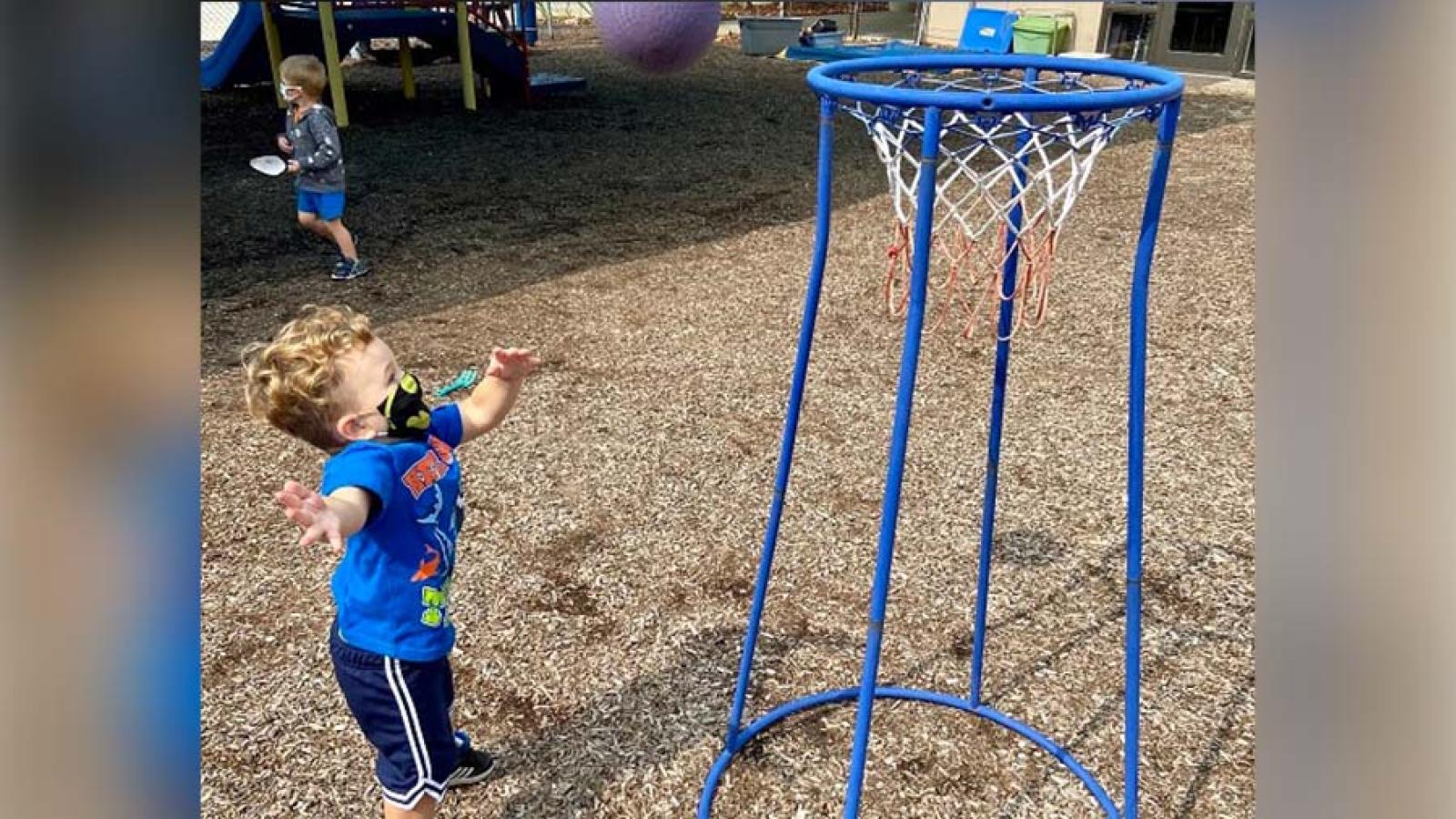 A child shoots a basketball into a small hoop.