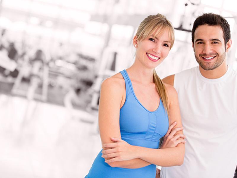 Photo of smiling man and women in a gym with the background black and white out. 