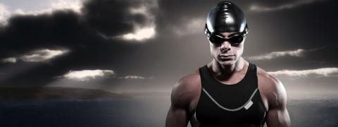 Photo of male swimmer with swim cap and goggles looking at the camera with dark sky