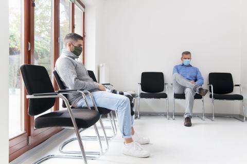 Photo of two men socially distanced in a waiting room wearing masks